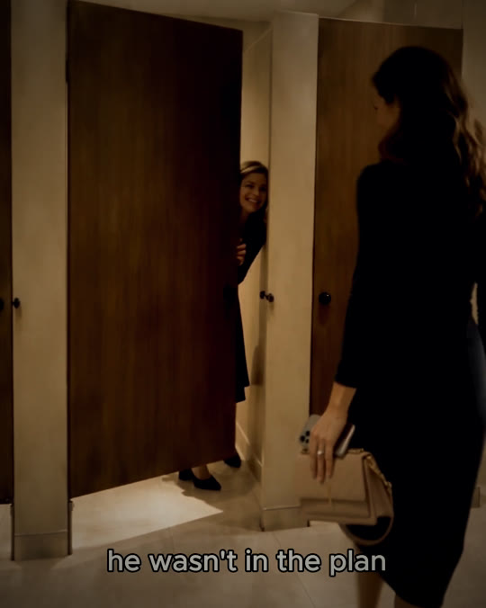 One friend peeks out of a stall as the other walks away